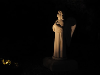 Close-up of an angelic statue bathed in soft purple light with golden highlights.