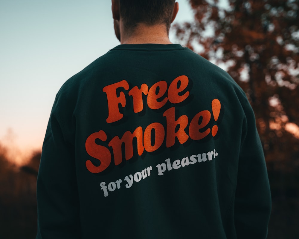 Ein Mann trägt ein kostenloses Rauchsweatshirt vor einem Baum