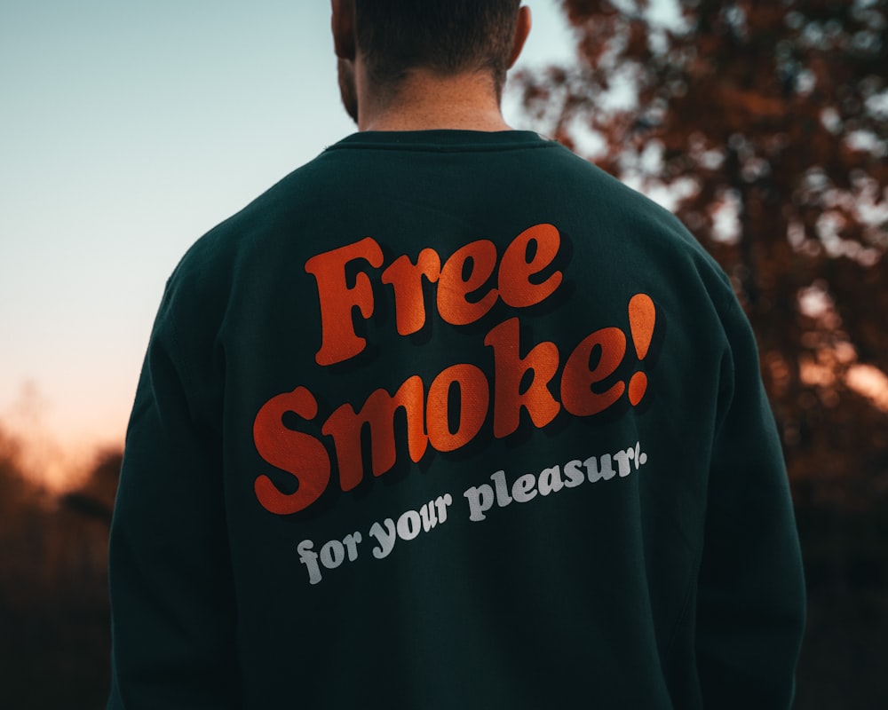 a man wearing a free smoke sweatshirt in front of a tree