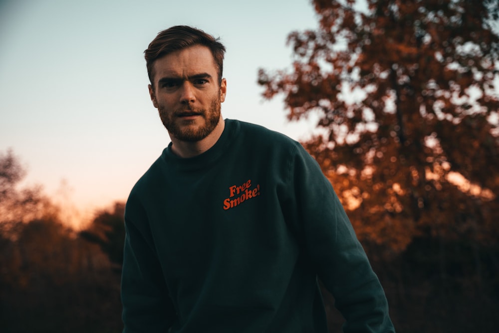 a man in a green sweatshirt standing in front of a tree