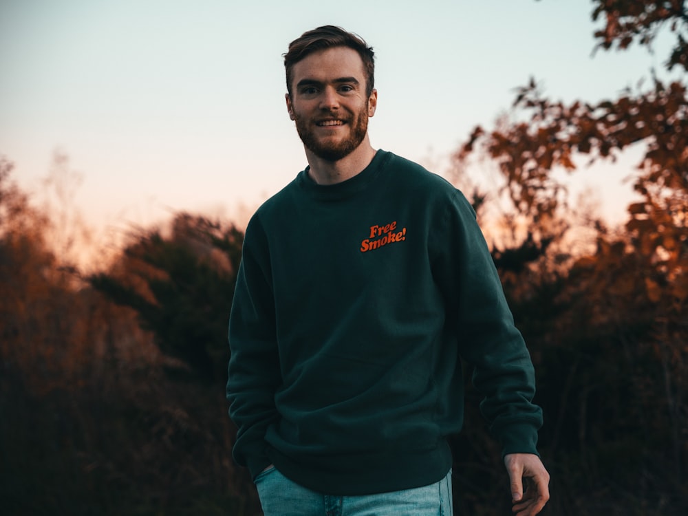 a man in a green sweatshirt standing in front of trees