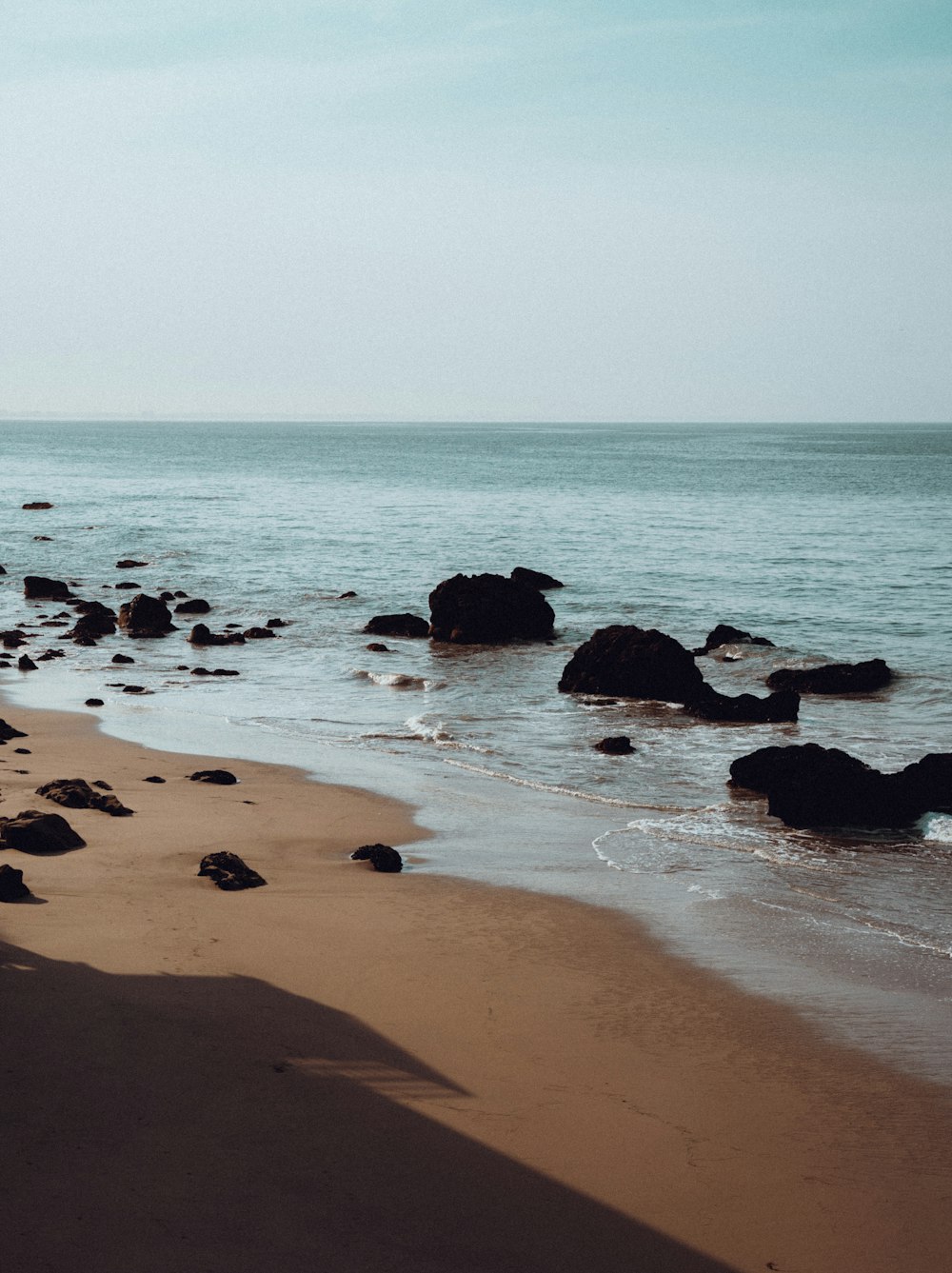 a sandy beach with rocks in the water