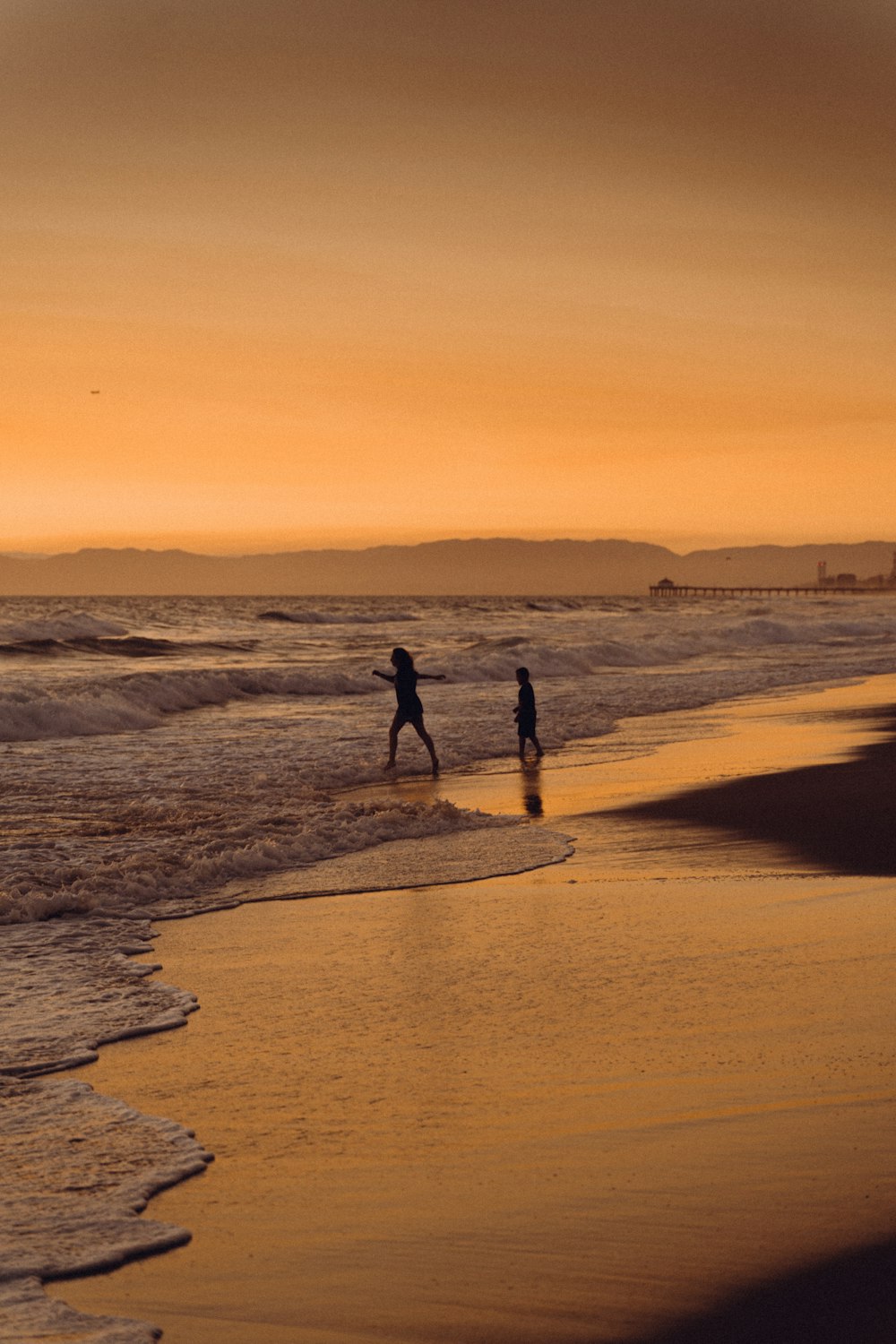 a couple of people walking along a beach next to the ocean