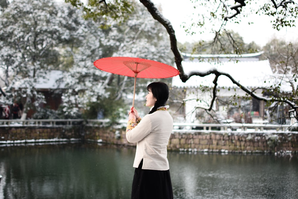 a woman holding a red umbrella in front of a pond