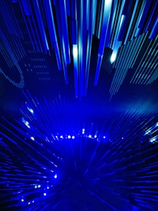 A dynamic and futuristic display featuring numerous elongated blue light beams arranged in a radiating pattern, creating a sense of movement and depth.