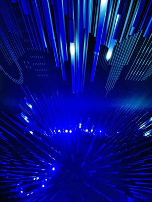 A dynamic and futuristic display featuring numerous elongated blue light beams arranged in a radiating pattern, creating a sense of movement and depth.