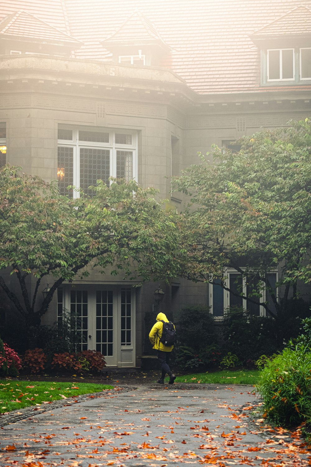 노란 재킷을 입은 사람이 집 앞을 걷고 있다