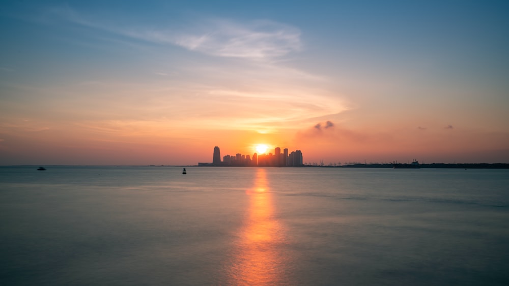 the sun is setting over the ocean with a city in the distance