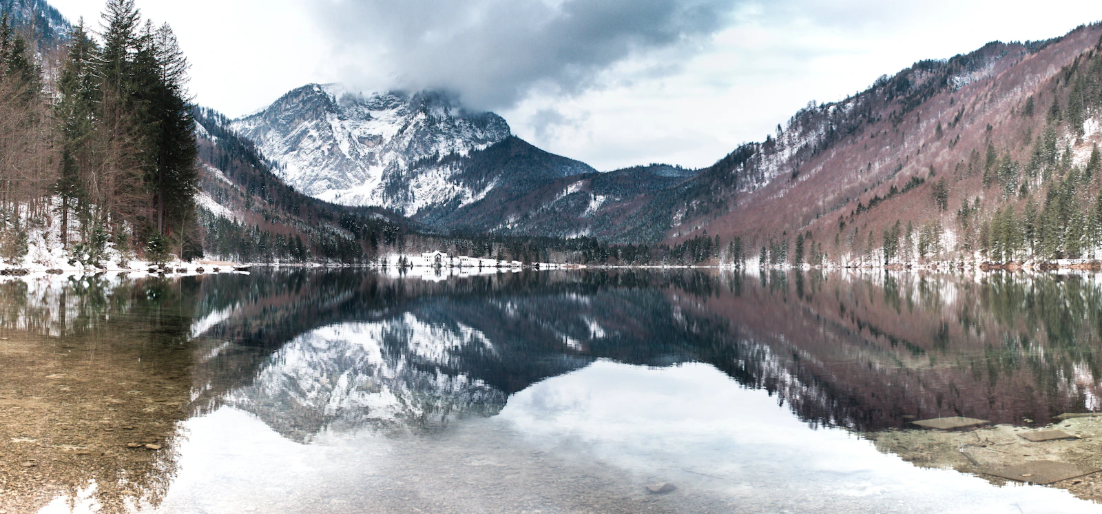 A winter lake lies beside snow-covered mountains and buildings.