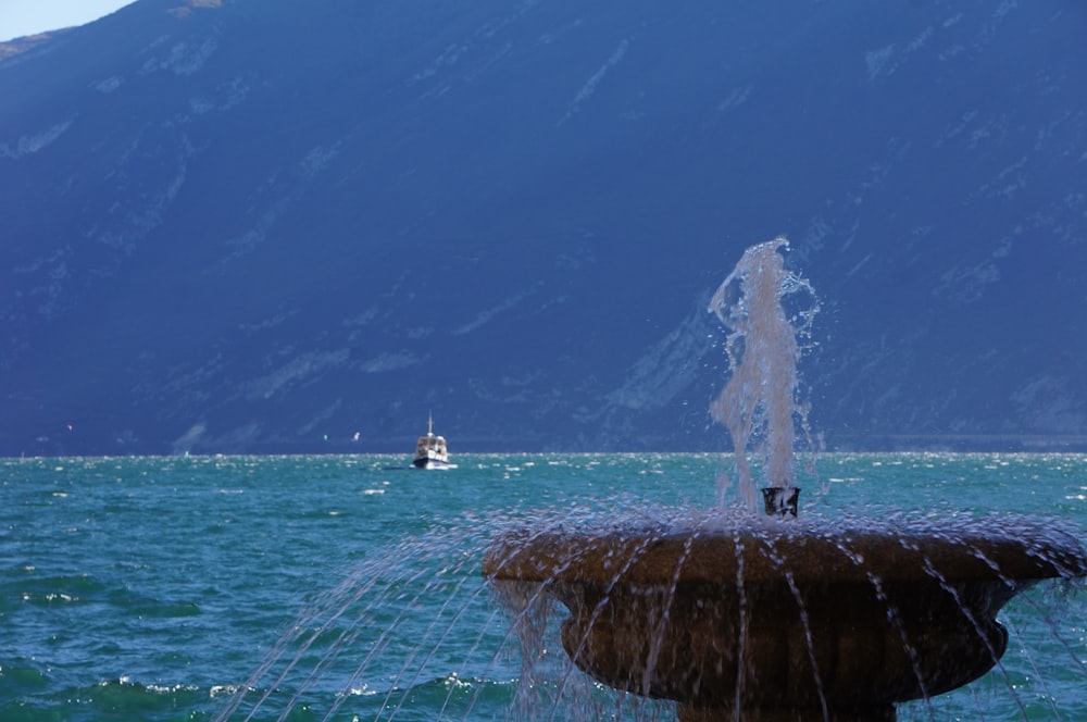 a fountain spewing water into the ocean with a boat in the background