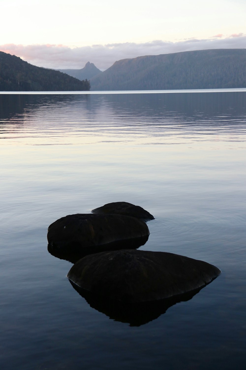 two rocks in the water with mountains in the background