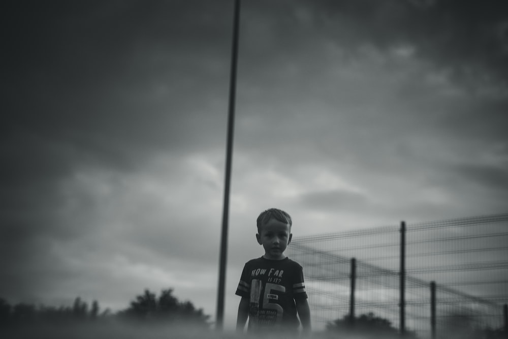 a young boy standing in front of a fence