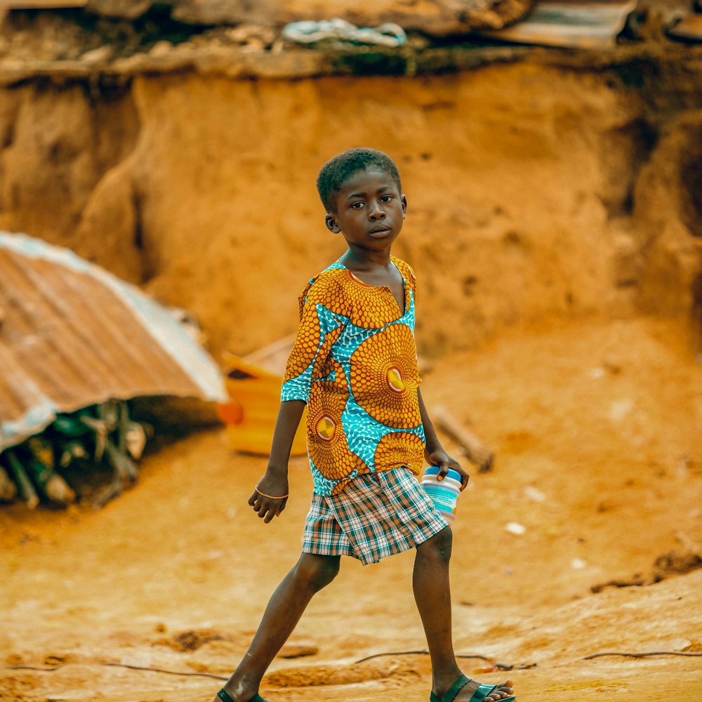 a young boy walking across a dirt field