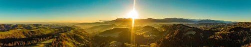 A panoramic view of the sun rising over the Alpes-Maritimes mountains with lush green forests