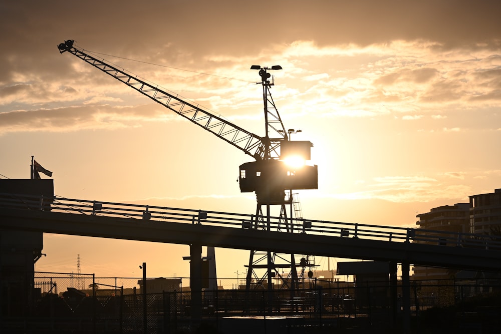 the sun is setting behind a crane on a bridge