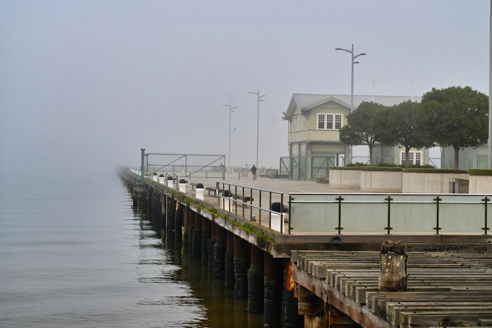 a long pier with a house in the background on a foggy day