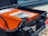 A close-up view of a hard plastic case with a latch open displaying an electronic device inside. The device is orange with a number of controls and indicators visible. Red and black cables or connectors are visible in the foreground, indicating potential use in electrical or technical applications.