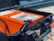 A close-up view of a hard plastic case with a latch open displaying an electronic device inside. The device is orange with a number of controls and indicators visible. Red and black cables or connectors are visible in the foreground, indicating potential use in electrical or technical applications.