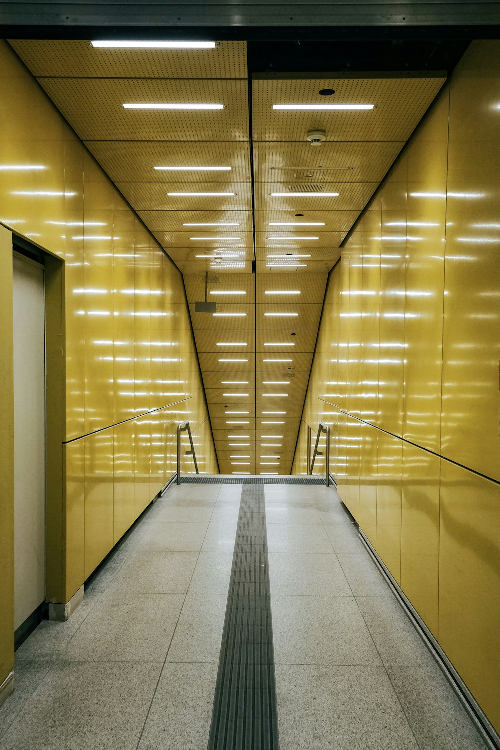 Un largo pasillo con paredes amarillas y una barandilla de metal