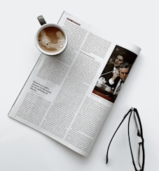 a cup of coffee sitting on top of a newspaper next to a pair of glasses