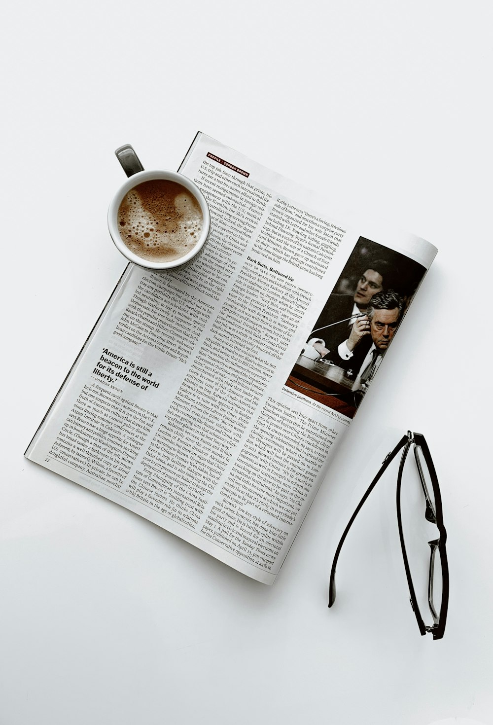 a cup of coffee sitting on top of a newspaper next to a pair of glasses