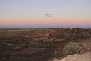 a view of a desert with a moon in the sky