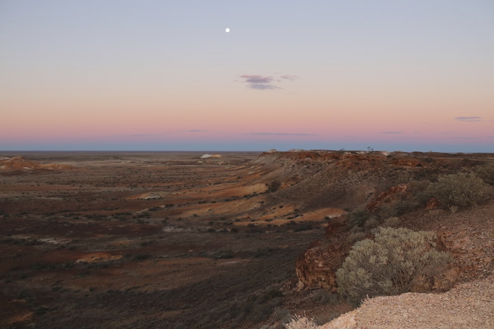 a view of a desert with a moon in the sky