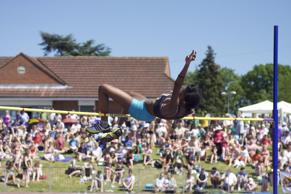 a woman jumping over a high jump in front of a crowd