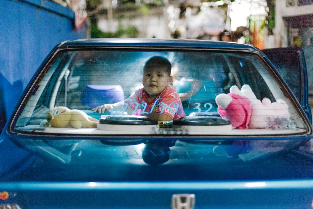 a small child sitting in the back of a blue car