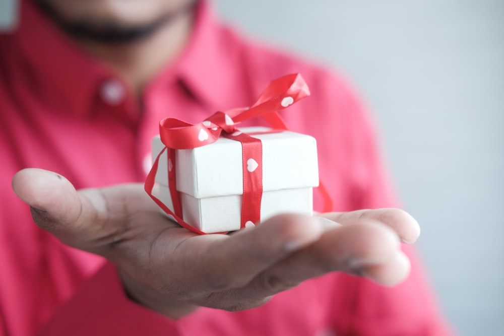 a man holding a white gift box with a red ribbon