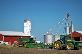 a tractor pulling a trailer with a grain silo in the background