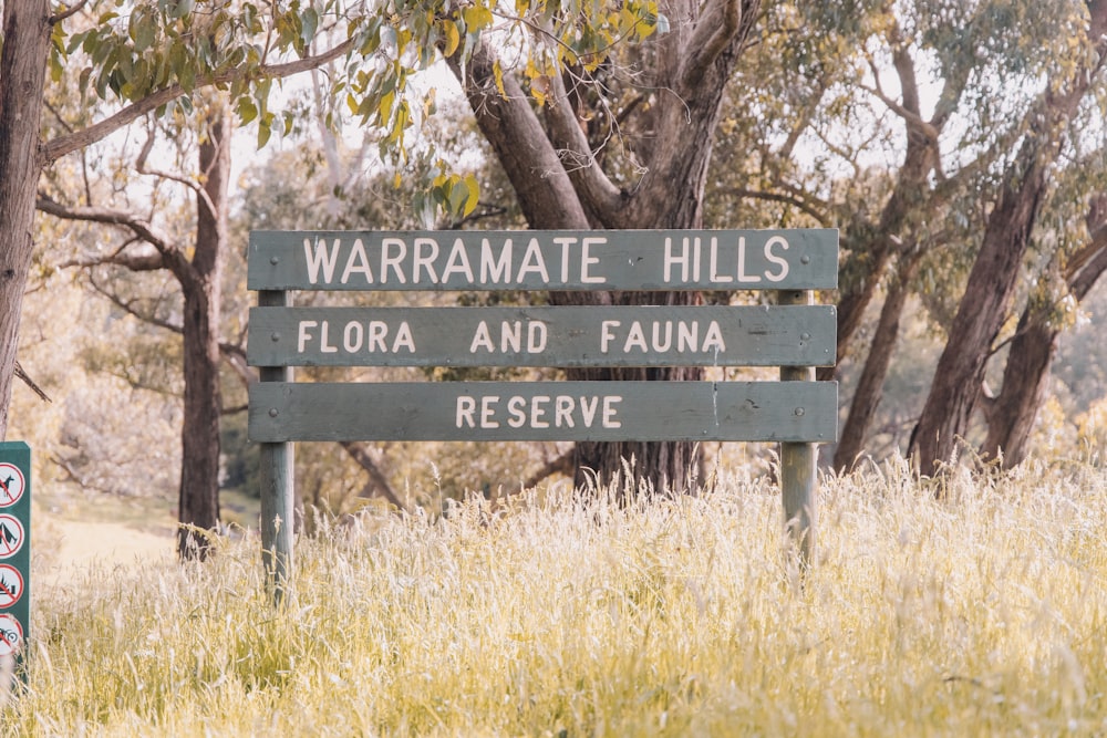 a wooden sign sitting in the middle of a grass covered field