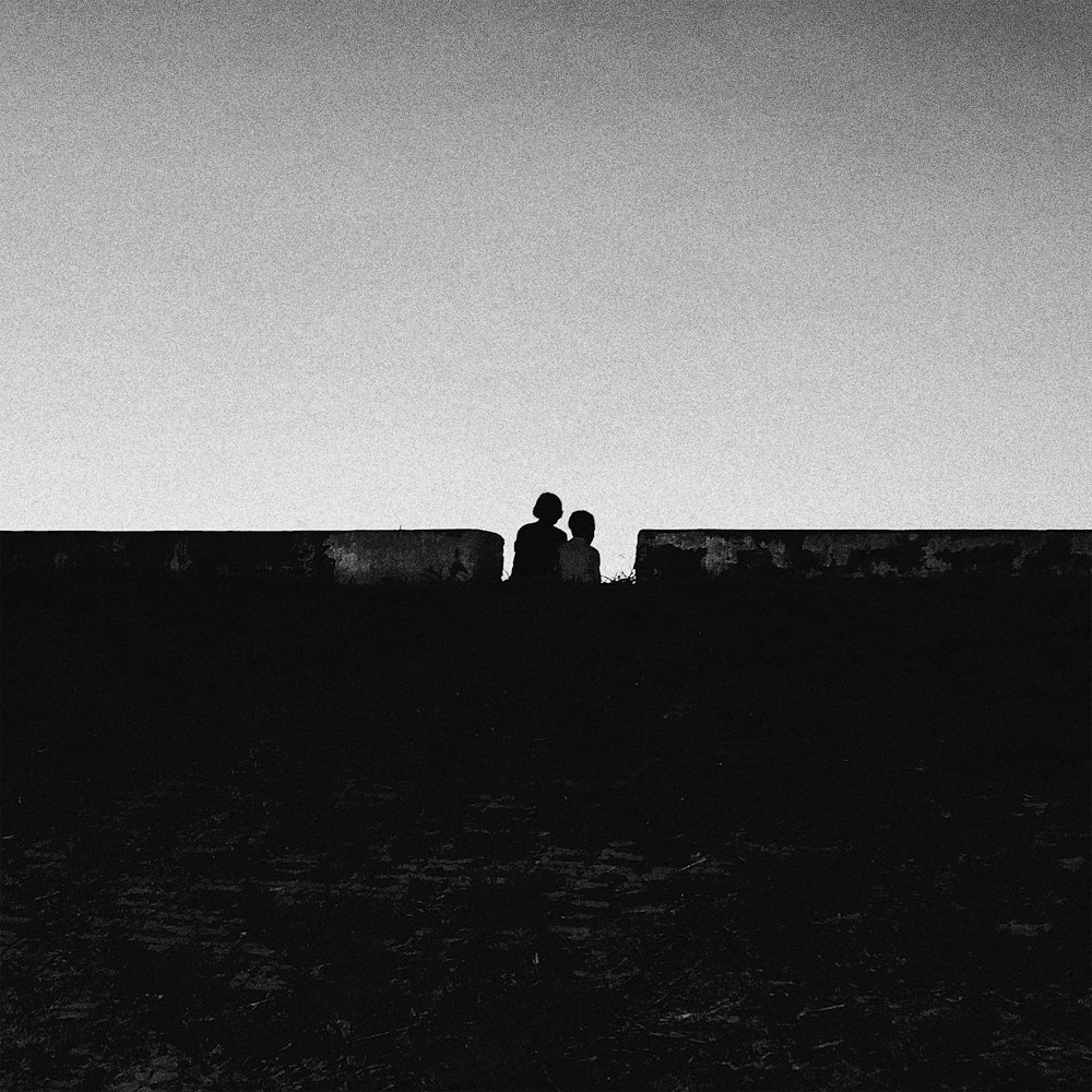 two people sitting on a wall looking at the sky
