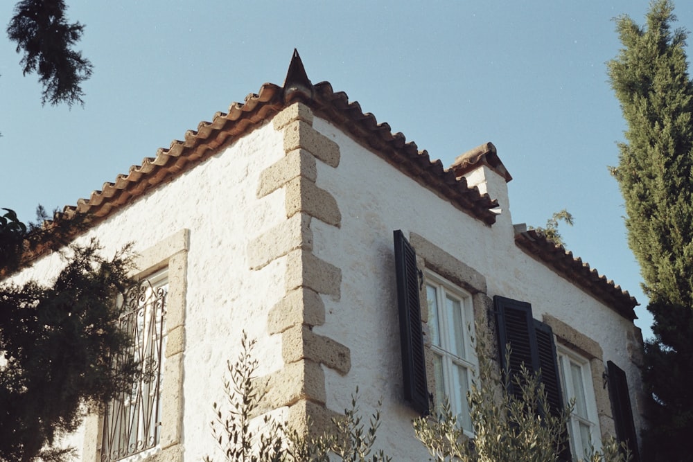 a white building with black shutters and a tree