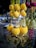 Vibrant decorative hanging items with golden and yellow tones, adorned with spherical plush elements and intricate metallic heart shapes. The background features hints of other colorful decorations and an outdoor setting.