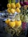 Vibrant decorative hanging items with golden and yellow tones, adorned with spherical plush elements and intricate metallic heart shapes. The background features hints of other colorful decorations and an outdoor setting.