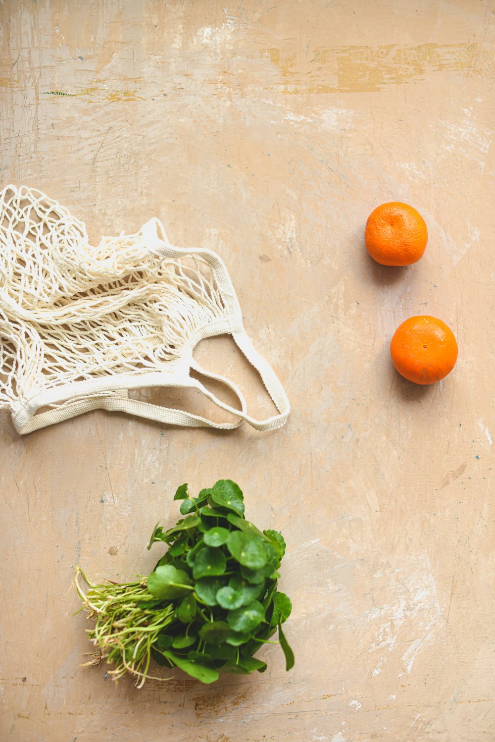 three oranges and a bag of greens on a table