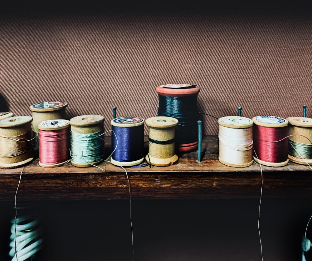 a row of spools of thread sitting on top of a wooden shelf