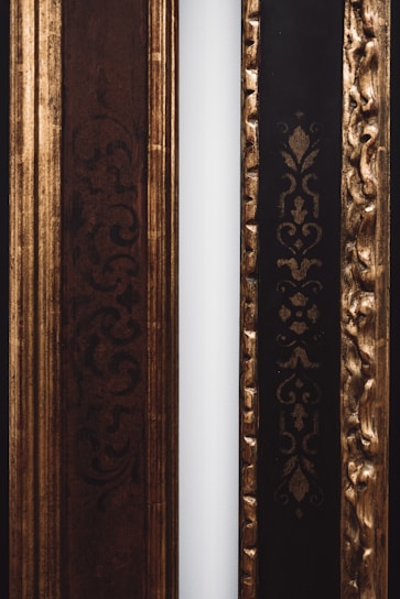 Two decorative frames with ornate patterns are positioned side by side. The left frame features intricate dark swirls and is primarily brown, while the right frame has an embossed gold pattern on a black background. A narrow white strip separates the two frames.