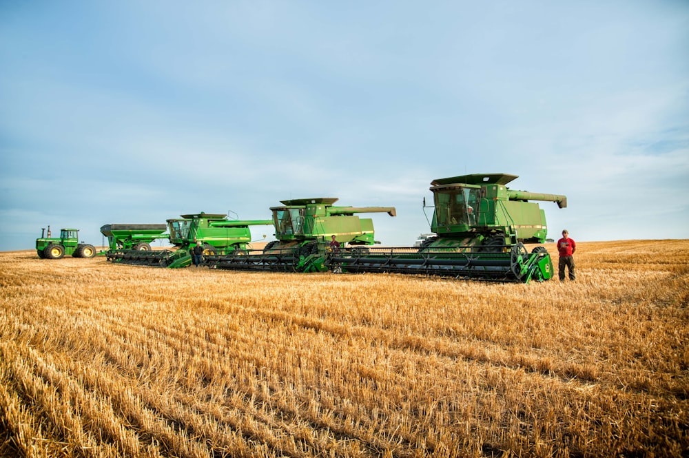 a man standing in a field next to a row of green farm equipment