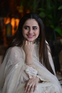 A confident woman wearing elegant semi-jewelry in soft olive and rose tones, smiling warmly.