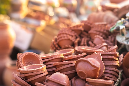 A collection of handcrafted clay oil lamps stacked closely together. The lamps, made from terracotta, have intricate designs etched into the surface, suggesting they are traditional artifacts used for celebrations or rituals.
