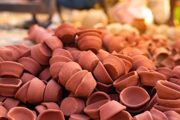 A pile of small, unglazed clay pots is neatly stacked. The earthen pots are reddish-brown, and their coarse texture is visible. The smooth, rounded shape of each pot is consistent, suggesting they were crafted by hand or using a simple mold.