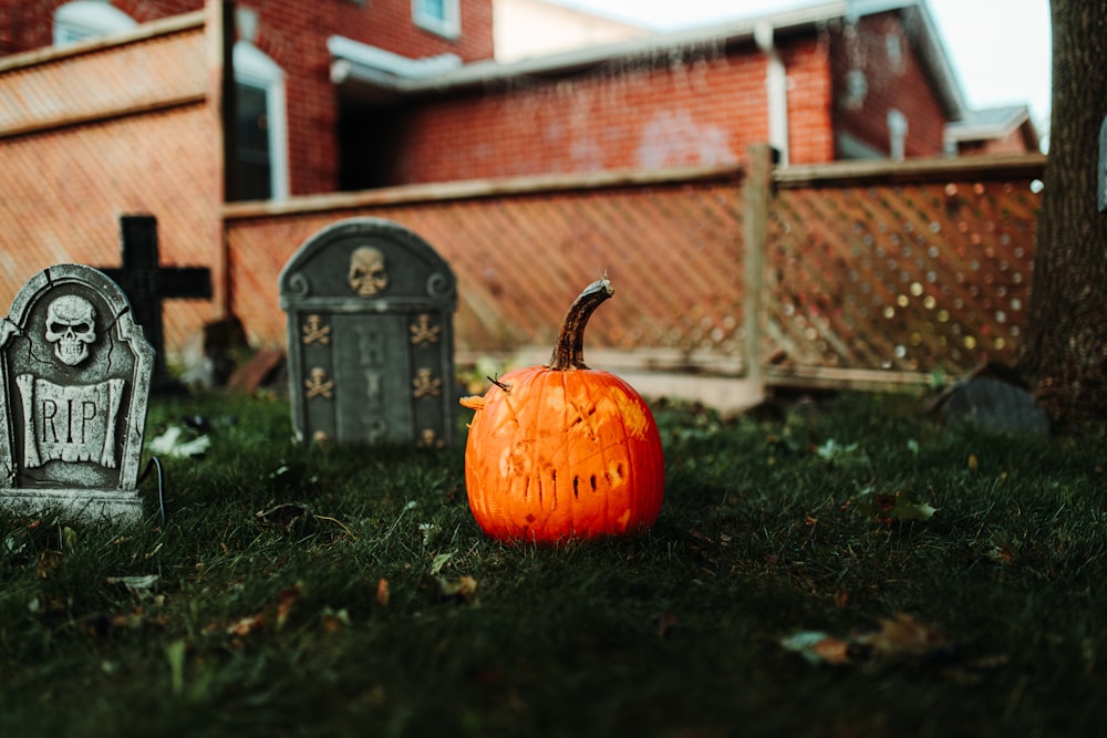a pumpkin sitting in the grass next to a tombstone