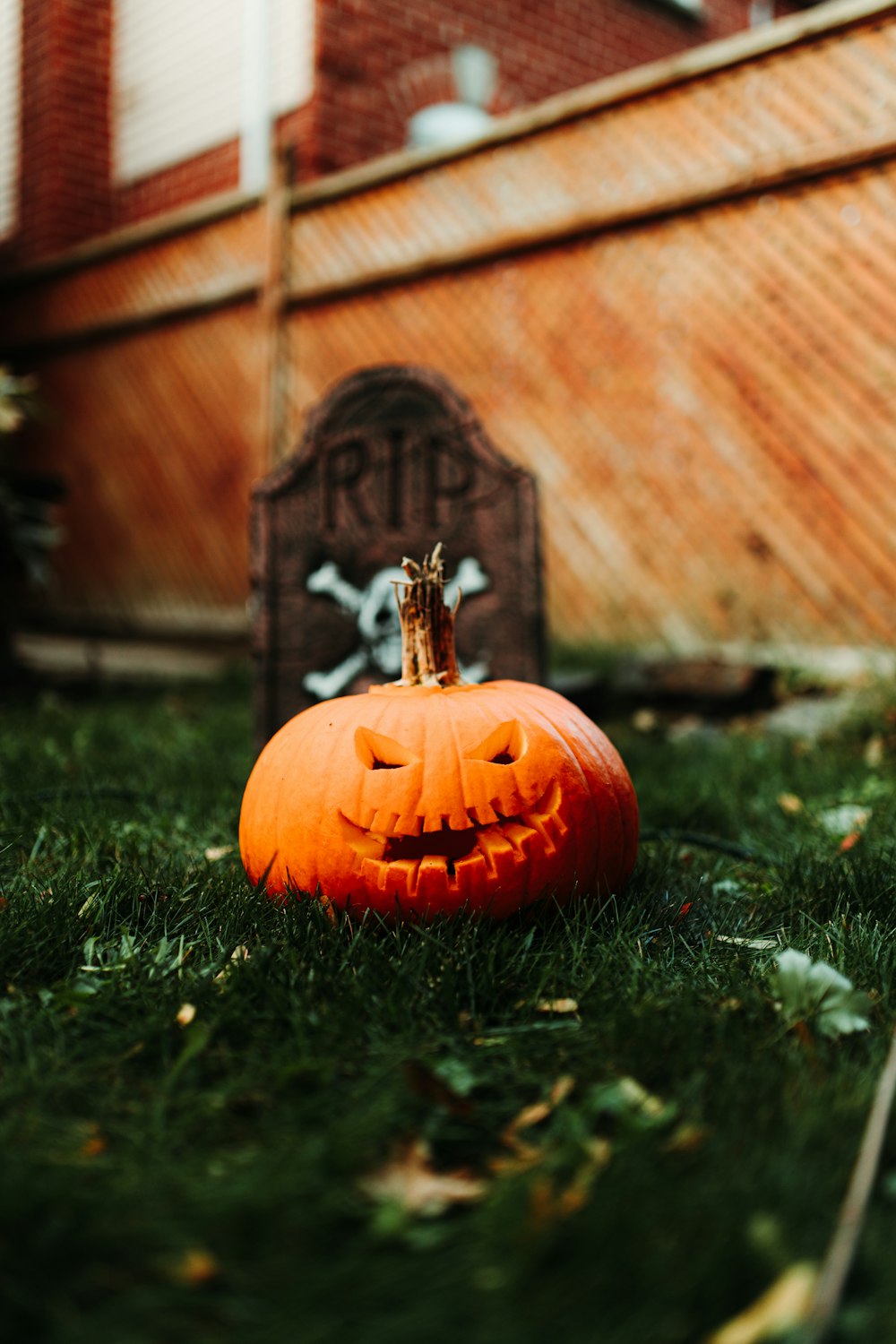 a carved pumpkin sitting in the grass next to a tombstone