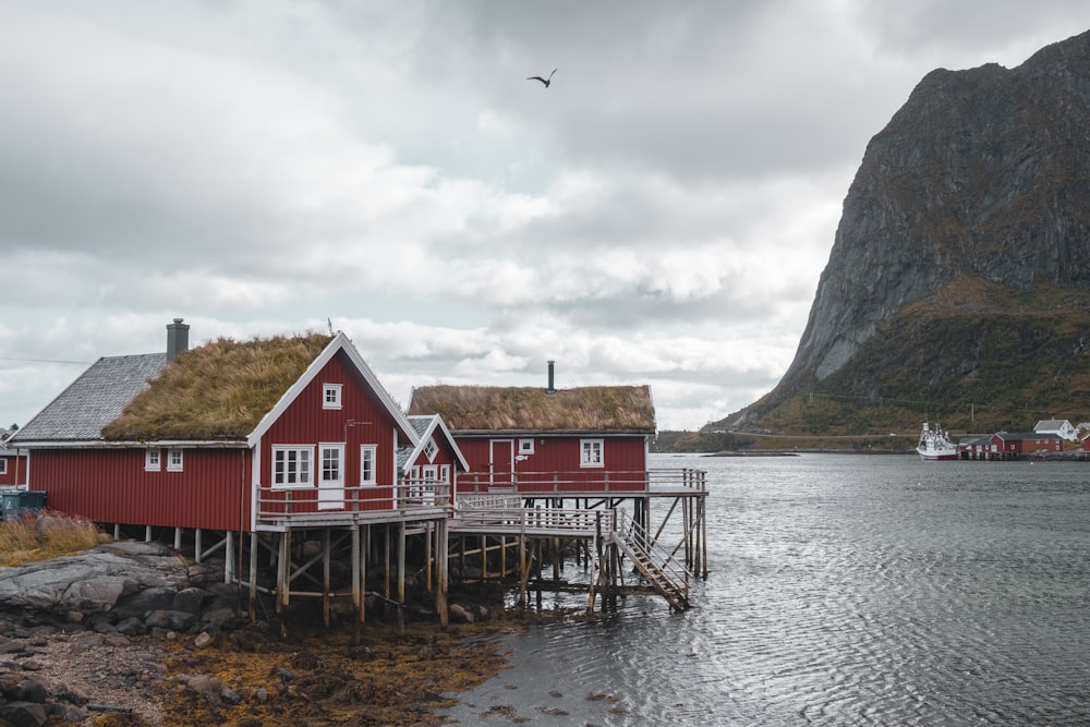 a red house with a grass roof next to a body of water