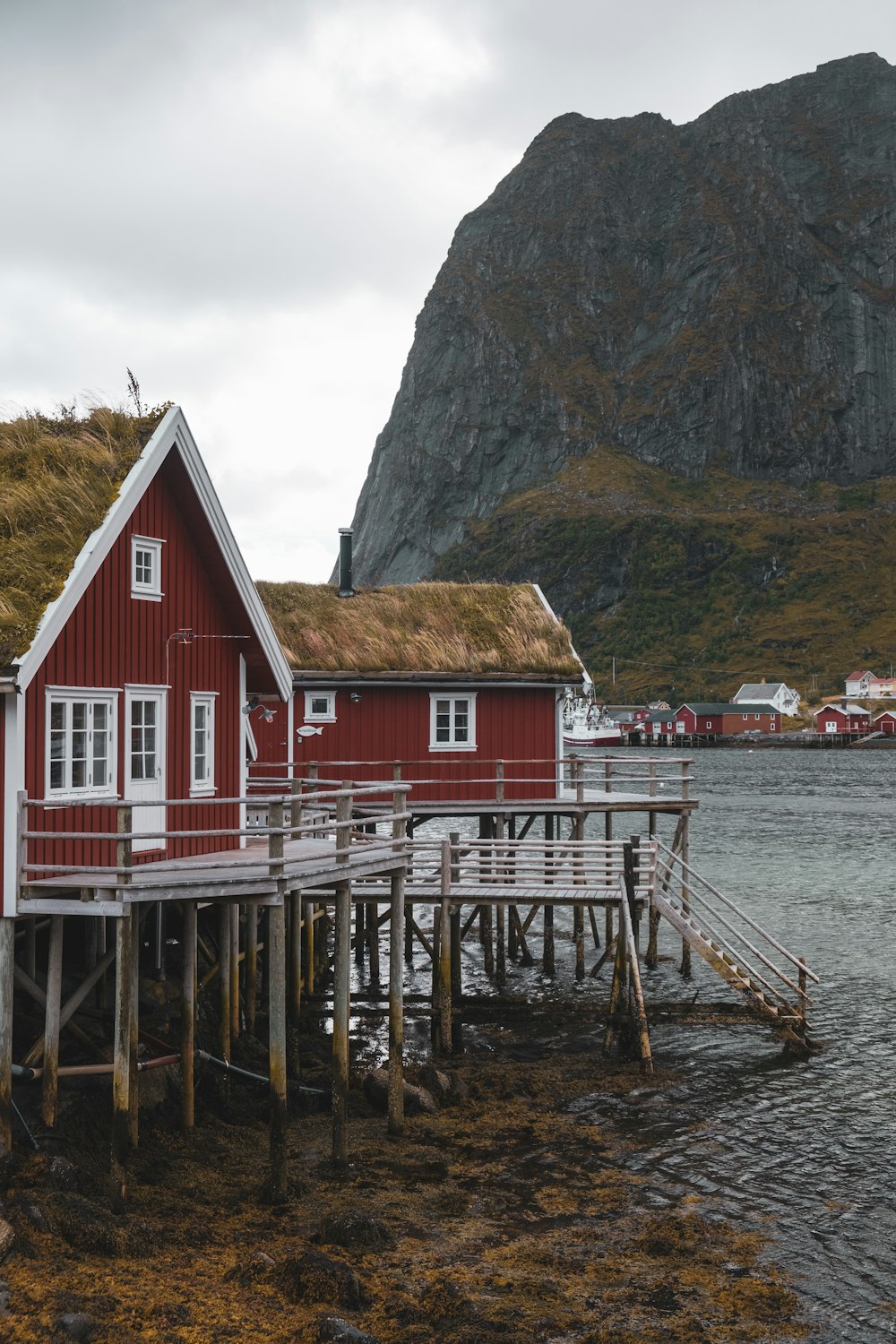 a red house with a grass roof next to a body of water