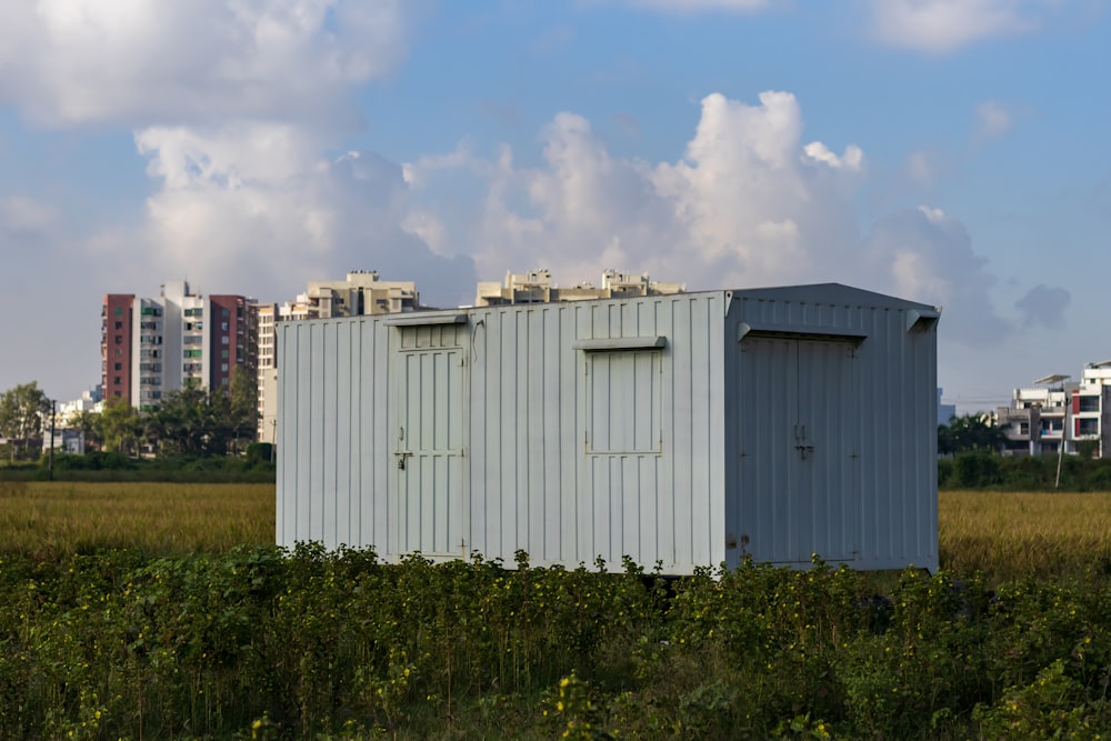 Una letrina blanca en un campo con edificios al fondo