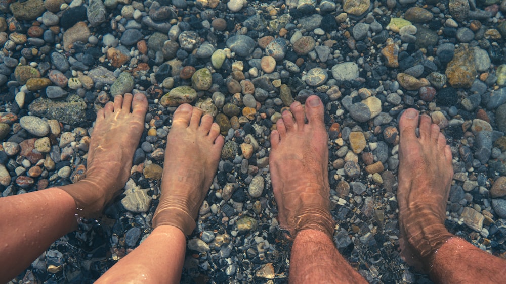 two people standing on a rocky beach next to a body of water