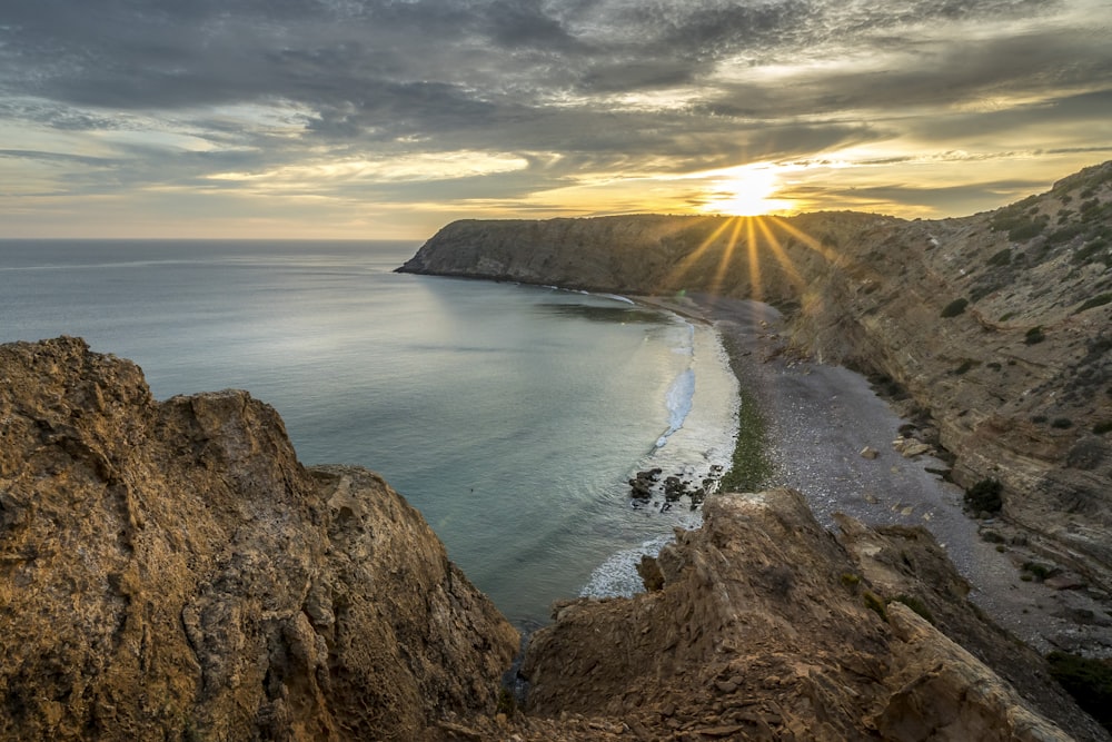 the sun is setting over a rocky beach